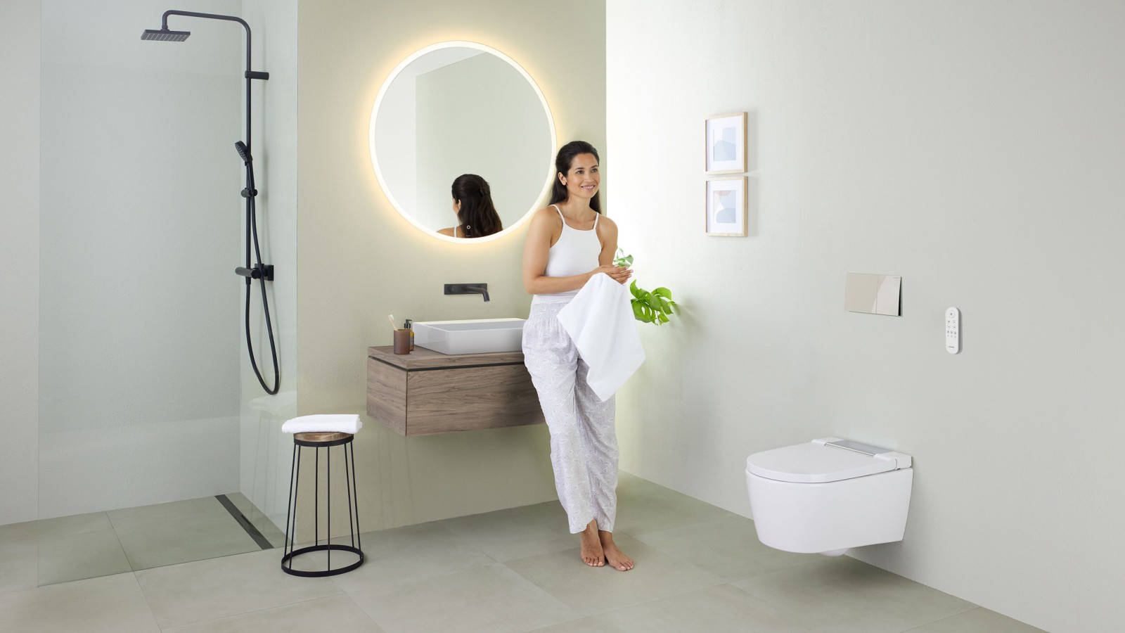 Geberit AquaClean Sela 비데 변기 및 Geberit VariForm 세면기 및 가구를 설치한 욕실에서 세면기에 기대어 있는 여성